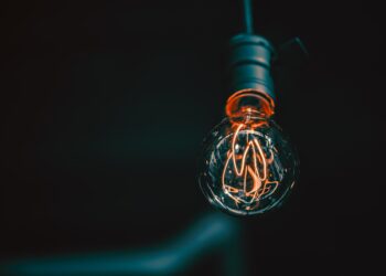 A close-up of a glowing Edison-style light bulb with visible filaments, hanging from a dark fixture against a black background—illuminating the innovative potential of Fintech Solutions. | FintechZoom