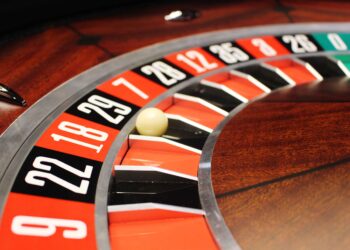 Close-up of a roulette wheel with a white ball resting in the slot for the number 18, surrounded by alternating red and black numbered sections. | FintechZoom