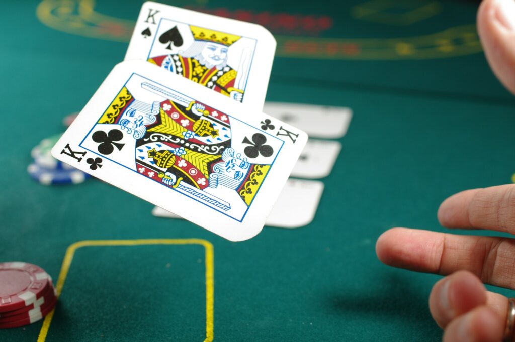 A hand tosses two playing cards, both kings, onto a green poker table with poker chips and other cards visible in the background. | FintechZoom