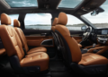 A spacious car interior with brown leather seats, a panoramic sunroof, and modern dashboard, shown from the side with a scenic waterfront view visible through the windows. | FintechZoom