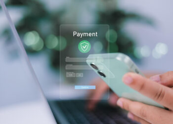 A person holds a smartphone and uses a laptop, filling out a digital payment form with card number, expiration date, CVV, and confirm button. Blurred green background suggests using Pay Later Apps while keeping personal data safe when using Buy Now options. | FintechZoom