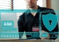 A man sits at a desk using a laptop and holding a credit card. Digital graphics highlight cybersecurity and online payment safety, suggesting how financial institutions can strengthen access controls for better security. | FintechZoom