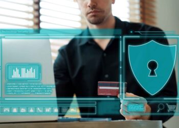 A man sits at a desk using a laptop and holding a credit card. Digital graphics highlight cybersecurity and online payment safety, suggesting how financial institutions can strengthen access controls for better security. | FintechZoom