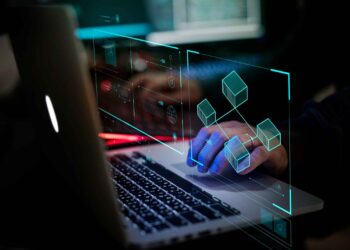 Person typing on a laptop with digital graphics of blockchain cubes and data charts overlaying the screen.
