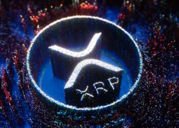 A glowing 3D XRP logo surrounded by colorful, sparkling particles in a circular formation.