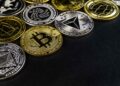 Various physical cryptocurrency coins, including Bitcoin and Ethereum, arranged on a black background.