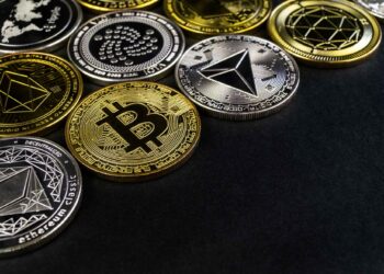 Various physical cryptocurrency coins, including Bitcoin and Ethereum, arranged on a black background.