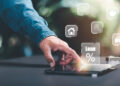 A person touches a tablet displaying virtual icons related to financial services, including a house, graduation cap, car, and a "Loan %" symbol, suggesting online loan or finance management. | FintechZoom