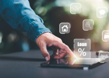 A person touches a tablet displaying virtual icons related to financial services, including a house, graduation cap, car, and a "Loan %" symbol, suggesting online loan or finance management. | FintechZoom