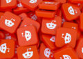 A pile of red square tiles, each featuring the white Reddit alien logo, stacked and scattered closely together in various orientations. | FintechZoom
