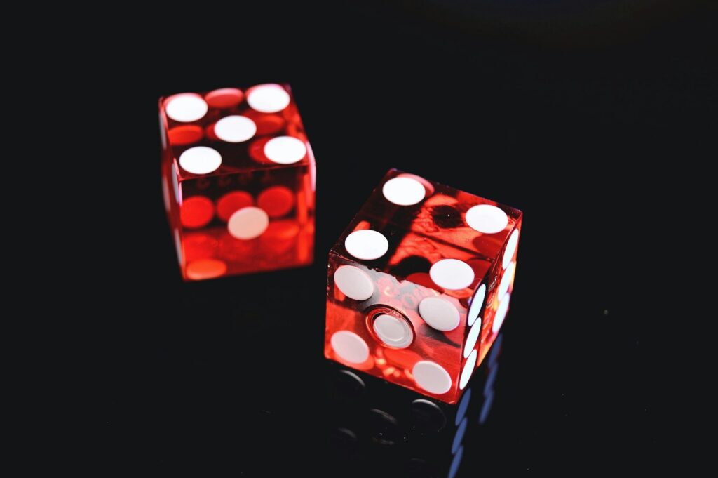 Two translucent red dice with white dots are placed on a glossy black surface, with one die showing the number six and the other showing the number five. | FintechZoom