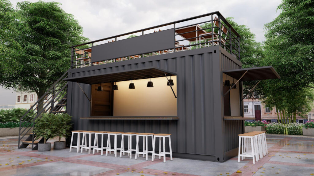 A modern shipping container restaurant café features a sleek black exterior, a serving counter with white bar stools, rooftop seating, and lush green trees surrounding the area. | FintechZoom