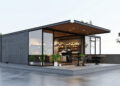 A modern Shipping Container Restaurant coffee shop featuring large glass walls, outdoor seating with black chairs and tables, potted plants, and a minimalist rooftop setting with a few small trees. | FintechZoom