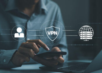 A person using a smartphone and laptop, with virtual icons showing a user, shield with "VPN," and a globe, representing secure internet browsing through a VPN connection. | FintechZoom