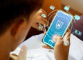 A person holds a smartphone displaying a security lock icon, surrounded by digital icons representing online banking, shopping, and global financial transactions, highlighting secure mobile banking. | FintechZoom