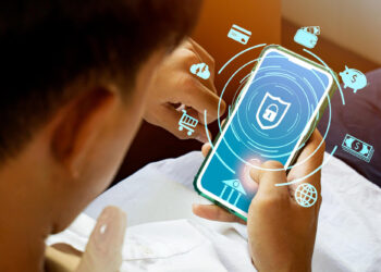 A person holds a smartphone displaying a security lock icon, surrounded by digital icons representing online banking, shopping, and global financial transactions, highlighting secure mobile banking. | FintechZoom