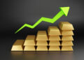 Stacks of gold bars arranged in ascending order with a bright green upward arrow above them, symbolizing growth or an increase in value. The background is dark and minimalistic. | FintechZoom