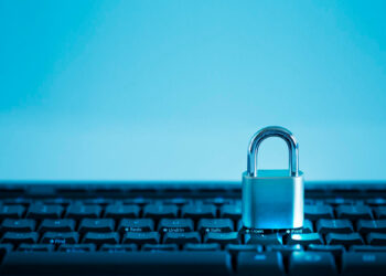 A silver padlock sits on top of a black computer keyboard, symbolizing cybersecurity and data protection, with a blue gradient background. | FintechZoom