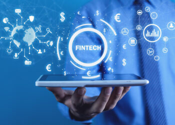 A person in a suit holds a tablet with digital graphics above it, including the word "Fintech," currency symbols, charts, and a globe, representing financial technology and global finance. | FintechZoom