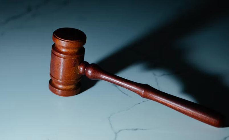 A wooden judge's gavel rests on a smooth, light-colored marble surface, casting a shadow to the side. | FintechZoom