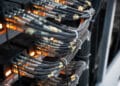 Close-up of several bundles of network cables connected to a server rack, with orange indicator lights glowing, illustrating data transmission or network infrastructure in a server room. | FintechZoom