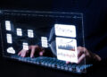 Person typing on a keyboard with virtual data analytics and database interface graphics projected in front, showing charts, graphs, and network diagrams in a dark environment. | FintechZoom