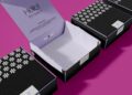 A set of black and white patterned boxes with open lids, revealing lilac interiors. One box lid reads "Hello! I’m here :)" on a purple background. The boxes are arranged on a bright pink surface. | FintechZoom