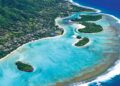 Aerial view of a tropical Cook Islands paradise with lush greenery, turquoise waters, coral reefs, and small islets near white sandy beaches, all bordered by the deep blue ocean. | FintechZoom