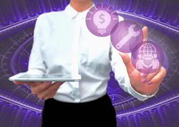 A person in a white shirt holds a tablet and touches floating purple icons, including a dollar sign in a lightbulb, a wrench, and people with a globe, with a digital abstract background. | FintechZoom