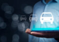 A person in a blue shirt holds a tablet with a glowing car icon above it, surrounded by faint car symbols, suggesting digital or online car services. | FintechZoom