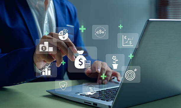 A person in a suit uses a laptop, with financial and investment icons such as dollar signs, graphs, coins, and targets digitally overlaid, representing financial planning or online banking. | FintechZoom