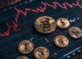 Several physical Bitcoin coins are placed on a digital screen displaying a red cryptocurrency price chart with fluctuating lines, symbolising market changes and Bitcoin trading activity. | FintechZoom