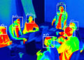 Thermal image of a group of people sitting around a table with laptops, each person’s face is highlighted with a box displaying their body temperature in Celsius. Colours range from blue (cool) to red and yellow (warm). | FintechZoom