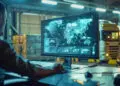 A person at a desk monitors a computer screen displaying global logistics data and maps in a warehouse with lorries and stacked boxes in the background, illuminated by industrial lighting. | FintechZoom