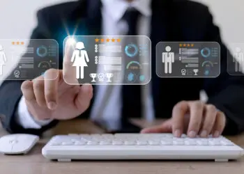 A person in a suit is using a keyboard and touching a virtual screen displaying digital profiles with icons, charts, ratings, and gender symbols, suggesting a concept of digital recruitment or employee evaluation. | FintechZoom
