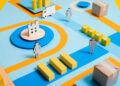 Colourful paper model of a supply chain with a factory, cardboard boxes, yellow blocks as goods, a delivery lorry, roads, and human figures on a blue background. | FintechZoom