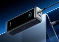 A black Anker power bank shows an 89% charge on its digital display while charging a laptop via a USB-C cable, set against a blue gradient background. | FintechZoom