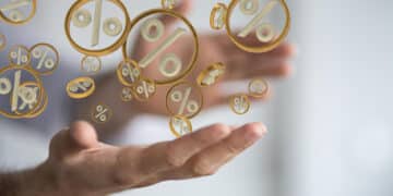 A person’s outstretched hands with floating golden percentage symbols between them, symbolising concepts like interest rates, finance, or discounts. The background is blurred, keeping focus on the symbols. | FintechZoom