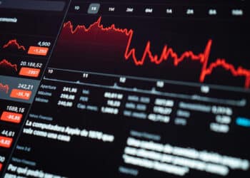A computer screen displays red graphs and financial data, showing significant declines in share prices and market values, with fluctuating lines and negative numbers indicating losses. | FintechZoom