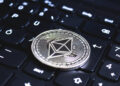 A silver Ethereum coin rests on a black computer keyboard, symbolising cryptocurrency and digital finance. | FintechZoom