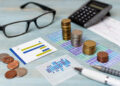 Stacks of coins, charts, a calculator, spectacles, and a pen on a desk, symbolising financial planning, accounting, or business analysis. | FintechZoom