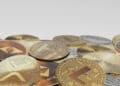 A pile of various cryptocurrency coins, including Bitcoin, Ethereum, Litecoin, XRP, and Tether, displayed on a white background. | FintechZoom