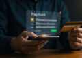 A person holds a credit card and mobile phone, processing an online payment on a virtual screen interface with payment details and a green Confirm button displayed. | FintechZoom