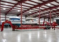 Large red boat trailer in a spacious indoor storage facility with several boats and scaffolding in the background under a high, red steel roof. | FintechZoom