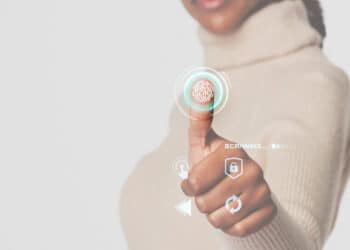A person in a beige polo neck uses their thumb on a virtual fingerprint scanner with digital security icons and the word “SCANNING...” displayed. | FintechZoom