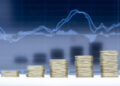 Stacks of coins arranged in ascending order in front of a blurred financial graph, symbolising growth and increasing profits. | FintechZoom