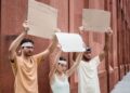 Three adults holding blank signs during a peaceful protest near a brick wall.