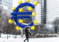 A person walks in snow past the Euro symbol in Frankfurt, Germany.