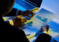 Two people in business attire reviewing financial charts and graphs on printed documents in a dimly lit office. | FintechZoom