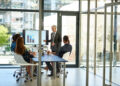 A man in a suit gives a presentation using a bar chart on a monitor to a group of colleagues seated round a conference table. | FintechZoom